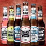 Sechs verschiedene Flaschen von MARX Städter Bier in einer Reihe auf einem Holzuntergrund.